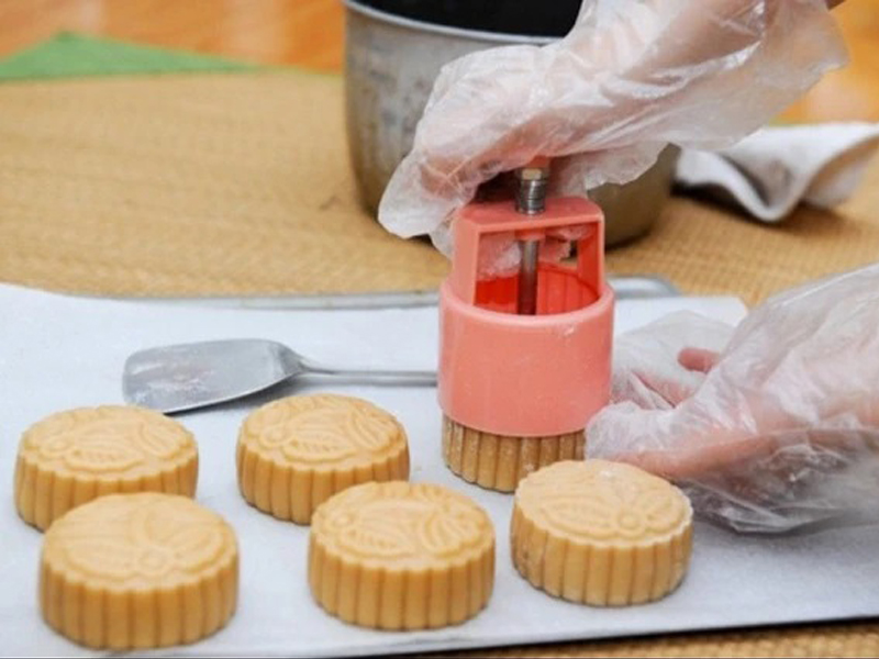 Đặt bột bánh Trung thu nhân đậu đỏ vào giữa khuôn gỗ, dùng tay ấn một lực vừa phải để bánh tràn đầy khuôn